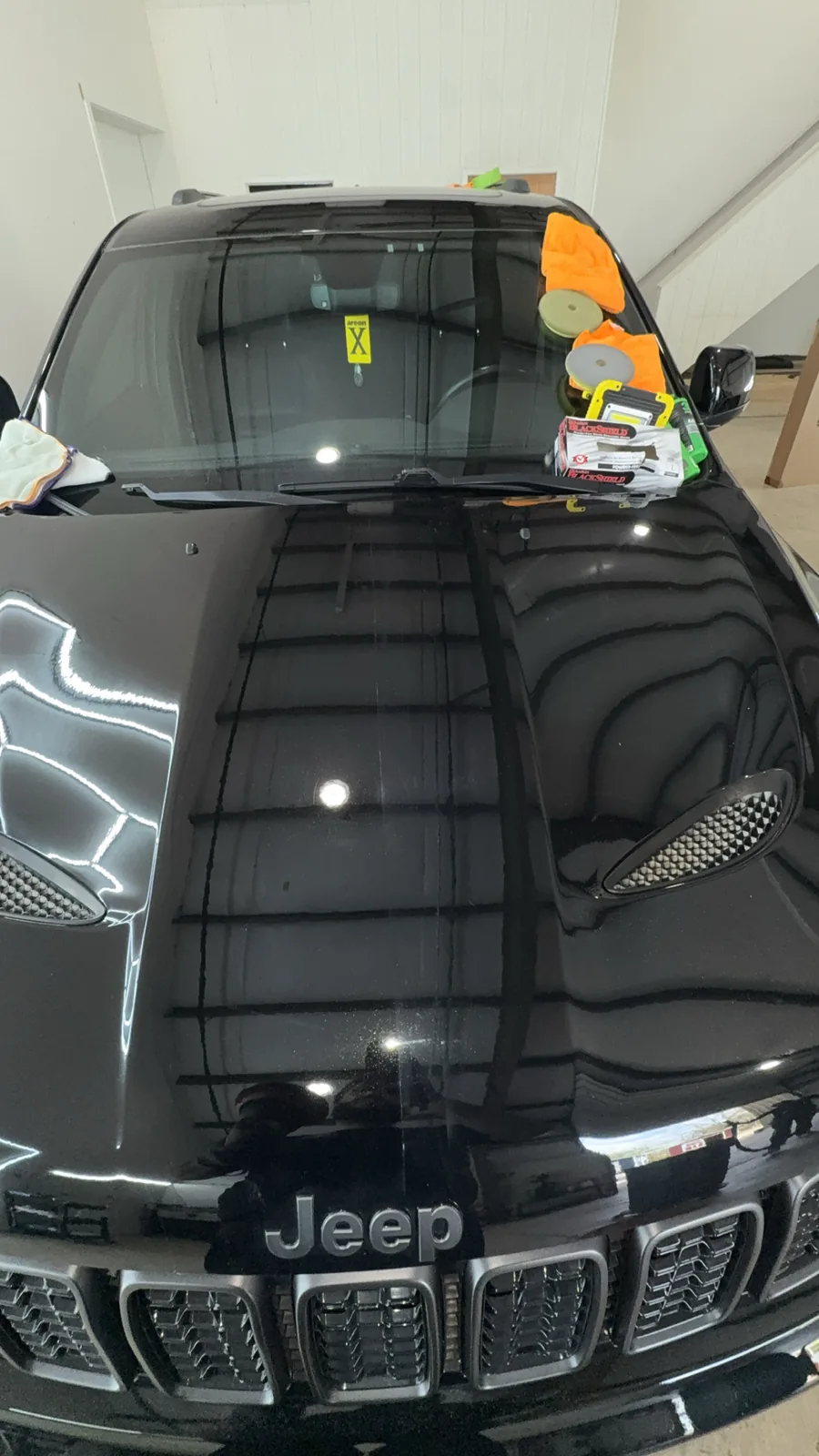 Black Jeep hood reflecting the shop's hex lighting, polishing pads and product on the cowl