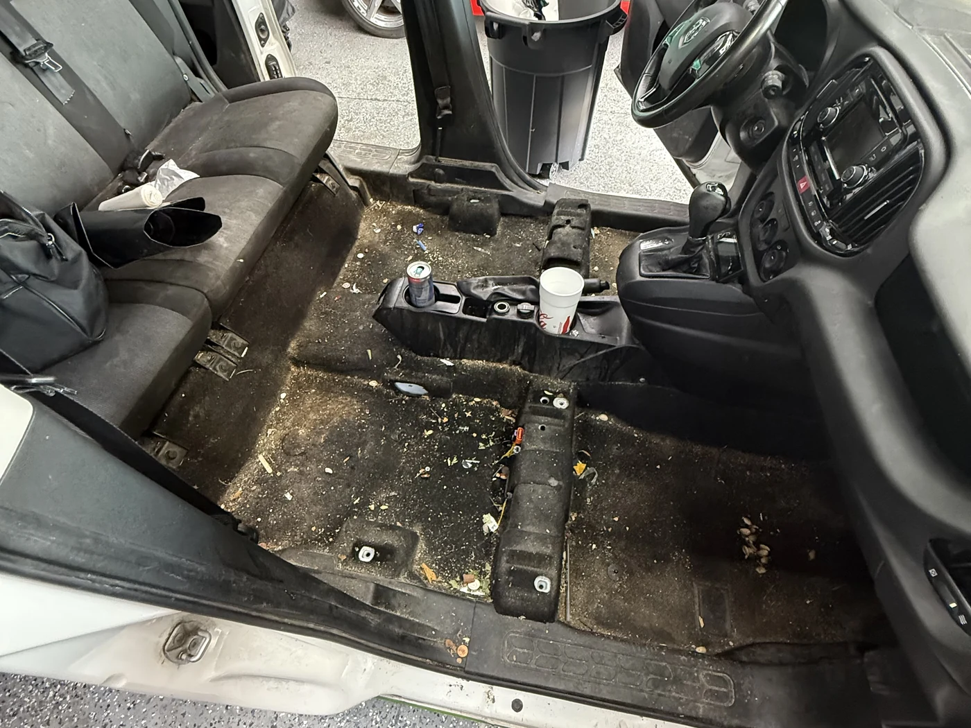 Car floor with the seats removed, carpet covered in debris and staining