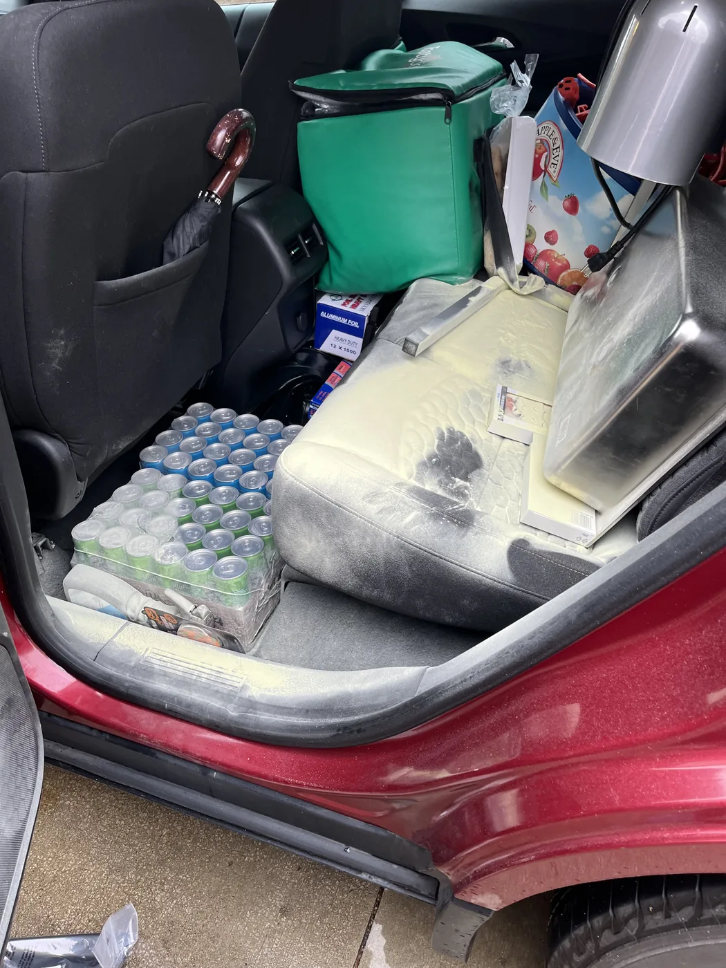Rear seat of a red car at check-in, loaded with a cooler, cases of water and boxes, seat stained