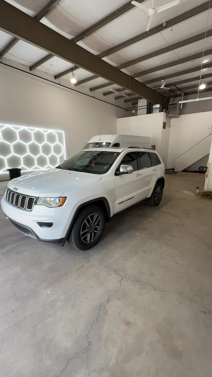 White Jeep Grand Cherokee parked under the shop's hex lighting