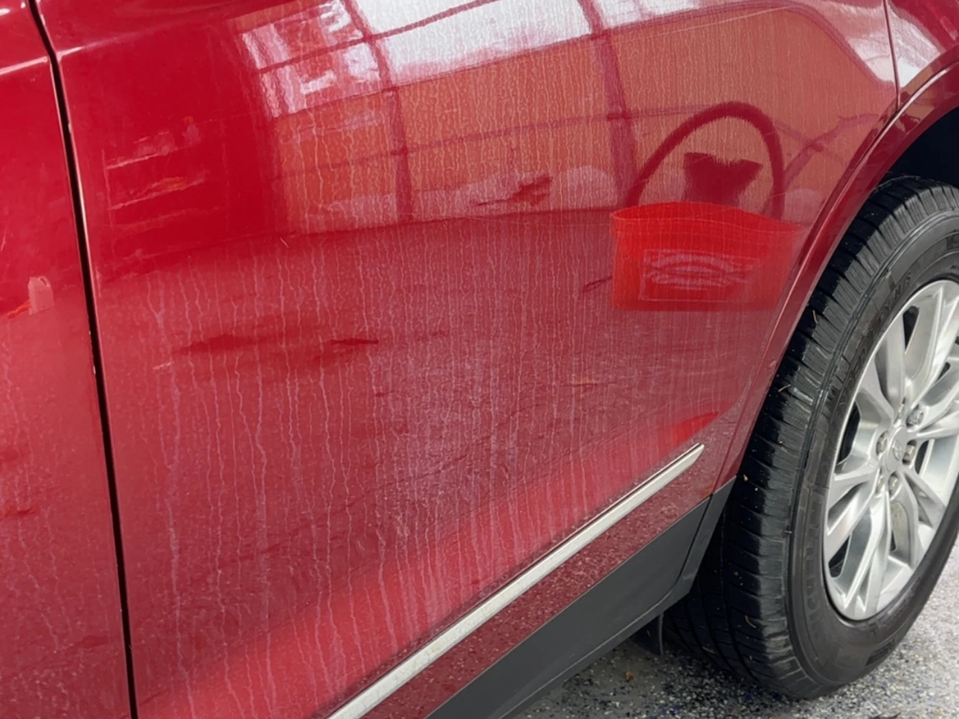 Red Cadillac door before correction, swirl marks and water spotting scattering the reflection