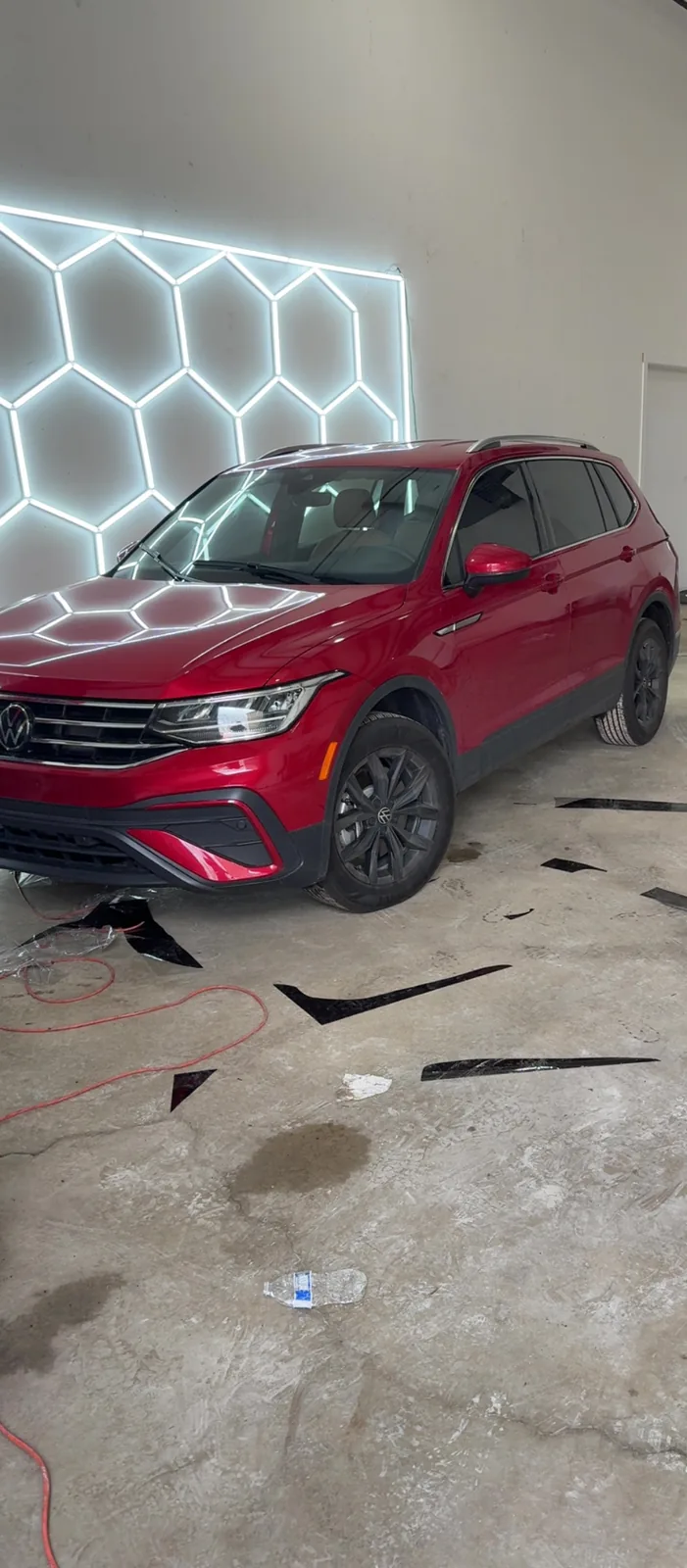 Red Volkswagen Tiguan with tinted windows in the A2 Auto Works bay, film offcuts on the floor